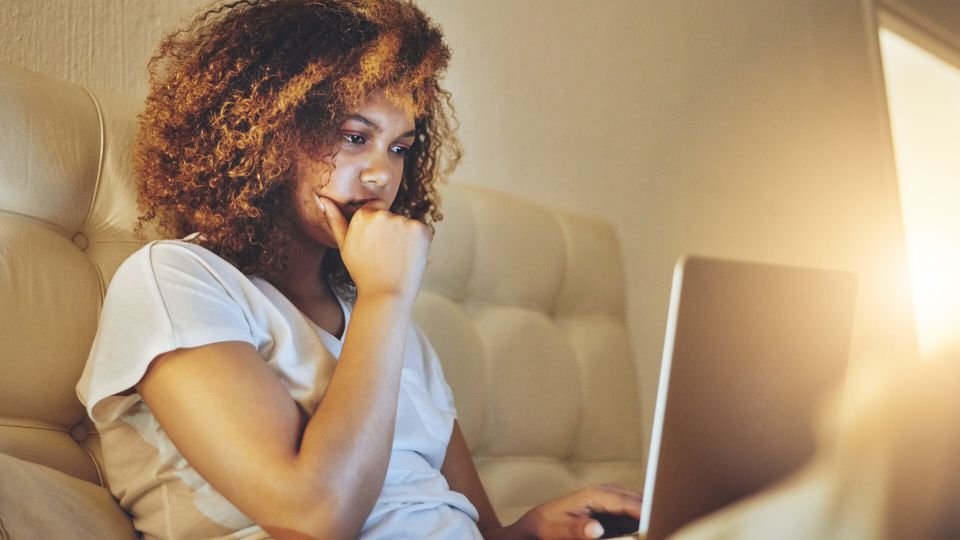 Shot of a young woman using a laptop while sitting on her bed at home.